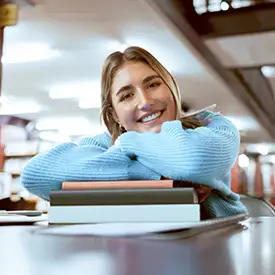 Glückliche Studentin sitzt mit ihren Büchern in der Bibliothek